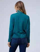 Polera de punto fino marca Nienty, color blanco, con cuello alto volcado y mangas largas con detalle de tajo en los puños.