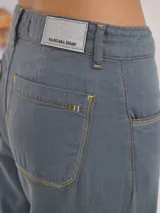 Pantalón gris de tiro medio alto, corte ancho, con bolsillos delanteros y traseros, detalles de atraques y triples costuras en color amarillo.