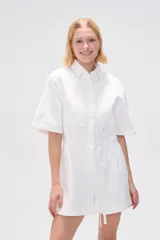 Mono corto blanco de algodón, con cuello camisero, cierre frontal con botones, mangas cortas y bolsillos.