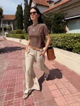 Pantalón marrón de lino con bordados blancos en los laterales y bolsillos. Corte recto y cintura con elástico.