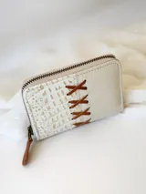 Billetera pequeña de cuero color crema, con cierre metálico y monedero interno. Presenta un diseño de cruces marrones en el frente y textura símil cocodrilo en un lateral.