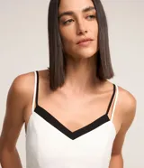 Blusa de breteles finos color blanco con escote en V y superposición contrastante en negro, confeccionada en crepé.