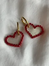 Par de aros colgantes con forma de corazón, con borde de strass rojos y aro superior plateado.