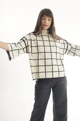 Sweater color crema con cuello alto y mangas cortas anchas, con diseño de cuadros negros.