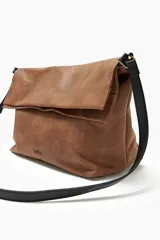 Bolso bandolera color tostado con correa negra y solapa con cierre magnético.