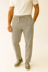 Pantalón de algodón a rayas verticales en tonos beige y negro, con bolsillos laterales, cintura elástica ajustable con cordón y corte ancho.