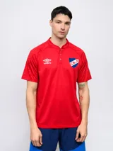 Remera polo de fútbol Umbro del Club Nacional de Football, color rojo con detalles geométricos en los hombros, cuello mao con botones y escudo del club bordado en el pecho.