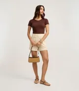 Blusa de algodón con textura acanalada en color blanco, de manga corta y cuello redondo. Presenta un acabado ondulado tipo festón con borde contrastante en color negro tanto en el cuello como en los puños de las mangas.