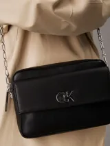Bandolera negra de cuero sintético con correa de cadena plateada y logo CK plateado en el frente.