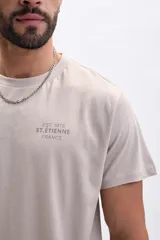 Remera de manga corta color taupe, con cuello redondo y estampado minimalista en el pecho que indica "EST. 1975 ST. ÉTIENNE FRANCE".