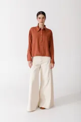 Blusa blanca de lino con cuello polo, manga larga y botones dorados. Presenta costuras a contratono en color naranja.