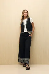 Pantalón negro de corte palazzo con bordado geométrico en el ruedo.