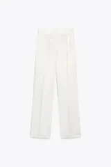 Pantalón blanco de tela satinada, tiro alto, corte ancho y pliegues en la parte delantera y trasera.