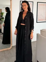 Camisa larga de seda negra, con cuello camisero, manga larga y cierre frontal de botones dorados.