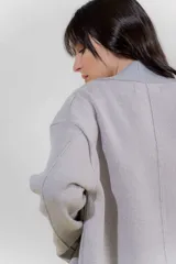 Chaqueta de punto color crudo con solapa ancha acanalada terminada con cadenetas en contraste negro. Tiene calce relajado, hombros caídos, largo a la cadera y manga larga.