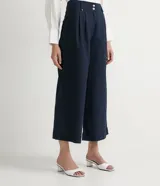 Pantalón pantacourt azul marino de lino y algodón, con cintura alta, pliegues delanteros, bolsillos laterales y cierre frontal con cremallera y botones.