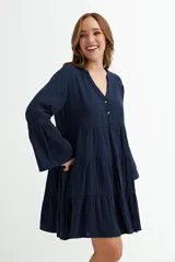 Vestido corto azul marino de manga larga con puños acampanados. Presenta un diseño escalonado con volados y escote en V con botones. El tejido parece ser de gasa o algodón texturizado.