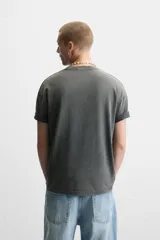 Camiseta gris de corte recto con cuello redondo y mangas cortas. Estampado ovalado con palmeras, sol y texto "Coconut Amora. Maui Offers Paradise".