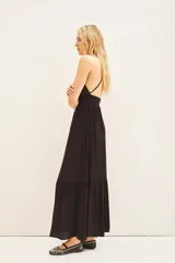 Vestido largo negro con breteles finos, aplique metálico en el escote, espalda baja con breteles cruzados regulables y cierre invisible en la cintura. Tiene un tajo central y volado ancho en el ruedo.