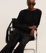 Suéter negro de poliéster con escote redondo y mangas largas. Presenta un diseño plisado en toda la prenda.