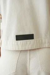 Campera de pana color blanco con cuello a la base, abotonada en el frente, entallada al cuerpo, fit corto y con dos bolsillos en la delantera.