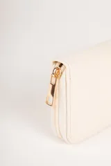 Billetera color beige con cierre de cremallera y apliques de tachas doradas en forma de corazón.