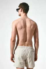 Short de baño color beige con textura de sirsaca, cintura elástica con cordón ajustable, bolsillos laterales y trasero ribeteado, aberturas laterales cortas y suspensor interior de malla.