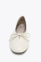 Zapato tipo bailarina color crema, de piel efecto soft, con detalle de lazo en la parte delantera y acabado en punta redonda.