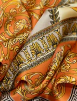 Pañuelo cuadrado de satén color naranja con estampado de motivos florales y grecas en tonos dorados, marrones y beige.
