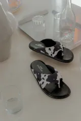 Sandalia tipo flip-flop con estampa cow print en blanco y negro. Presenta una tira ancha acolchonada que abraza el pie y una base negra lisa. Diseño liviano y cómodo de la marca Anne Chaussure.