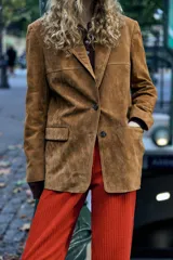 Blazer marrón de piel de ante, con cuello solapa, manga larga, bolsillos delanteros con solapa, forro interior a tono, abertura en la espalda y cierre frontal con botones.