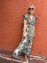 Vestido largo de seda color crema con estampado de hojas y flores en negro. Tiene escote en V cruzado, mangas cortas con volados y lazo ajustable en la cintura.