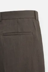 Pantalón de vestir color marrón oscuro, confeccionado en lino italiano. Presenta corte regular fit, cintura con pliegues, bolsillos laterales y traseros ribeteados, y terminación con dobladillo. Cierre frontal con cremallera y botón.