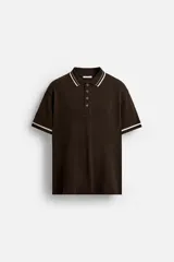 Polo marrón de punto canalé con cuello solapa, cierre frontal de botones a presión y manga corta con rib combinado a contraste en color blanco.