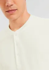 Camiseta color beige con cuello redondo abotonado y mangas cortas.