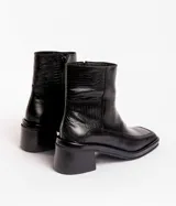 Bota corta de cuero charol negro, con caña baja, cierre lateral y taco cuadrado de madera.