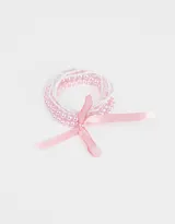 Set de cinco pulseras elásticas con cuentas de perlas rosas y blancas, unidas por un lazo de cinta de raso rosa.