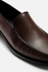 Mocasín de vestir color marrón oscuro, con capellada de cuero, suela a contraste y ligero tacón.