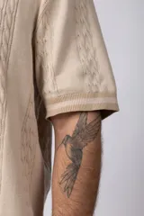 Camisa de tejido de punto color beige, con cuello tipo bowling, manga corta y corte relajado. Cierre frontal con botones.