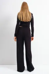Pantalón negro de corte ancho, tiro alto, con bolsillos traseros decorativos con botón dorado y pliegues delanteros.