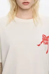 Camiseta de algodón color negro con efecto gastado (acid wash) y cuello redondo. Presenta un pequeño estampado en relieve color rosado en el pecho.