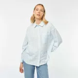 Camisa celeste y blanca a rayas verticales, de corte holgado, manga larga y bolsillo de parche en el pecho.