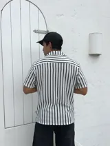Camisa tejida a rayas verticales blancas y negras, de manga corta y cuello solapa.