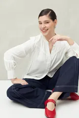 Camisa celeste de manga larga con cuello redondo y escote en V. Presenta detalles de pasamanería en el frente y las mangas, y botones forrados al tono. De corte fluido.