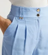 Pantalón cigarrete celeste de lino y algodón, con pliegues delanteros, bolsillos laterales, cintura con elástico en la espalda y cierre con botones metálicos.