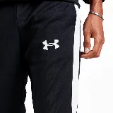 Conjunto deportivo Under Armour de hombre, compuesto por campera y pantalón de acetato negro con detalles de rayas blancas en mangas y laterales. La campera tiene cuello alto, cierre frontal y logo bordado en el pecho. El pantalón tiene cintura elástica con cordón ajustable y logo bordado en la cadera.