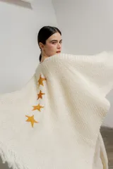 Ruana color crema de tejido grueso con flecos y apliques de estrellas doradas.