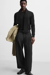 Pantalón negro de corte amplio tipo balloon fit, con cintura con pliegues frontales, bolsillos delanteros y traseros de plastrón. Cierre frontal con cremallera y botón.