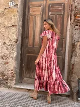 Vestido largo de seda con estampado tie-dye en tonos rojo y blanco, con mangas cortas con volados y ruedo con volados.