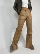 Pantalón de cuero color beige, corte jean, tiro medio-alto, con costuras a la vista y aberturas laterales en el ruedo.